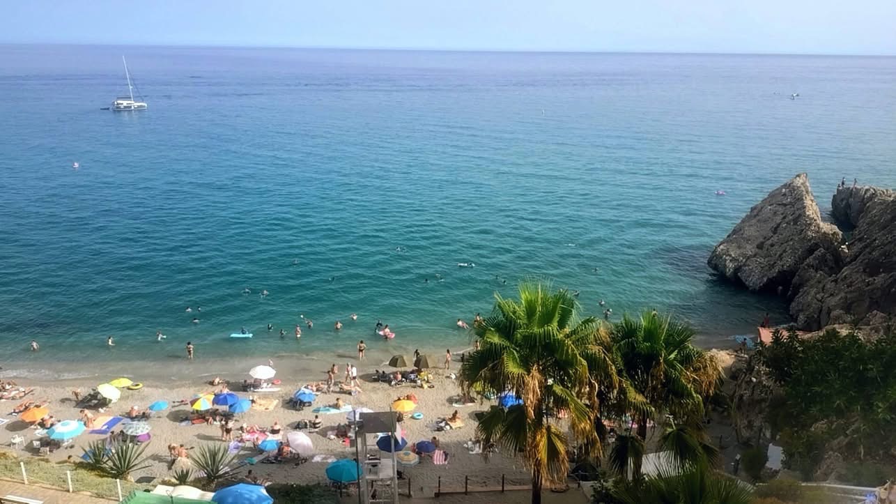 Overzicht van een druk strand met badgasten, rotsen