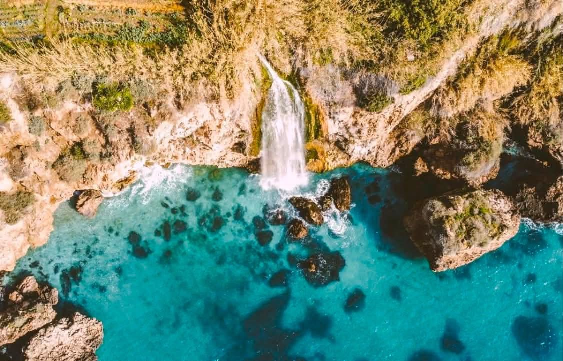 Vattenfall som störtar ned i det turkosa havet vid klipporna