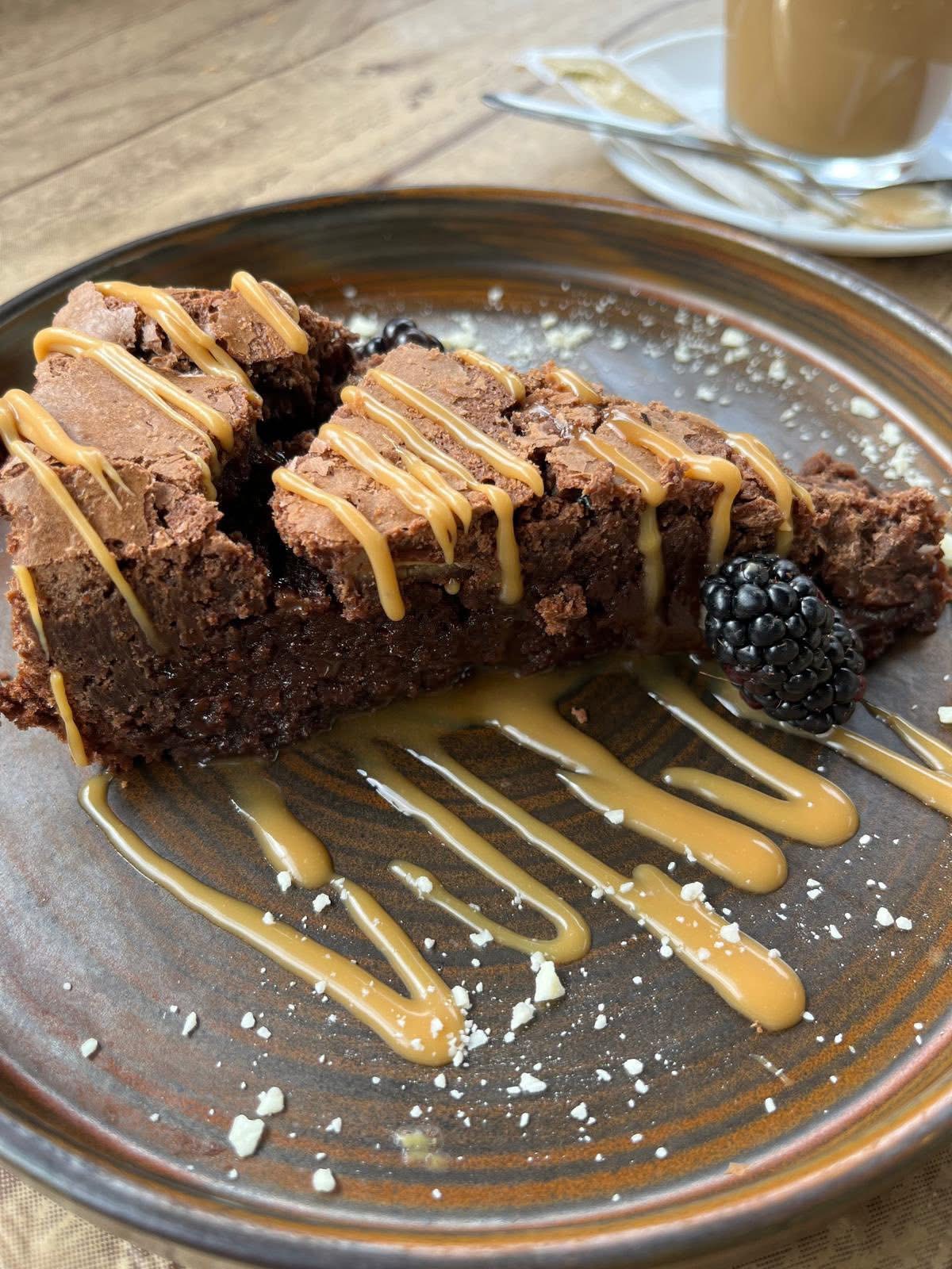 Brownie with caramel sauce and blackberry on a brown plate