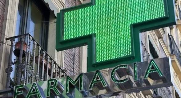 Cartel luminoso verde de una farmacia con la palabra 'FARMACIA' y una cruz.