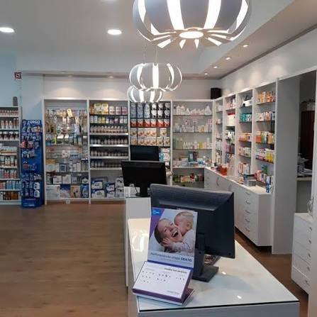 Interior de una farmacia moderna con estantes blancos llenos de productos y un mostrador con dos pantallas de ordenador y lámparas de diseño.